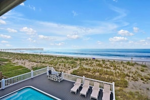 A pool area with lounge chairs and a view of the beach and ocean.