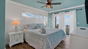 Une chambre à coucher avec un lit, des tables de chevet, un ventilateur de plafond et une vue sur l’océan.