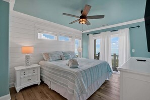A bedroom with a bed, nightstands, a ceiling fan, and a view of the ocean.