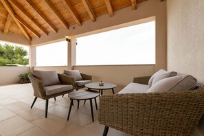 Un espacio de patio cubierto con mobiliario de mimbre, incluyendo un sofá y sillas, y una pequeña mesa redonda.