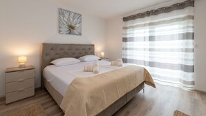 A neatly made bed with a headboard, bedside tables with lamps, and a large window with curtains. - Villa Zrilić (Benkovac)