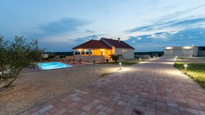 A house with a swimming pool, a paved driveway, and a well-lit exterior at dusk. - Villa Zrilić (Benkovac)