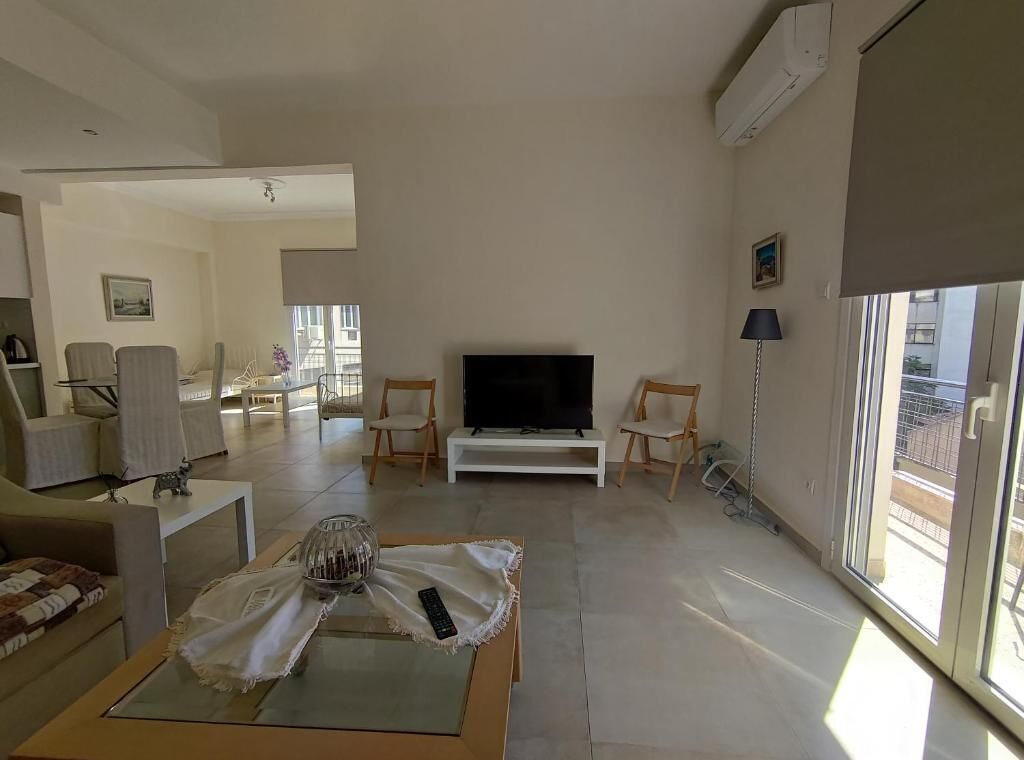 Een moderne woonkamer met een flatscreen televisie, comfortabele zitplaatsen en een groot raam dat natuurlijk licht binnenlaat.
