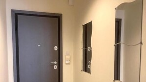 Un couloir avec une porte sombre, un interrupteur et un miroir accroché au mur.