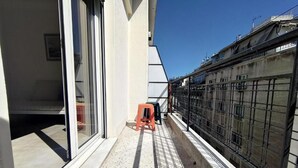 Un étroit couloir extérieur doté d’un sol carrelé, d’un petit tabouret orange et d’une clôture métallique d’un côté.