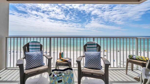 Ein Balkon mit zwei Stühlen und einem kleinen Tisch, mit Blick auf einen Strand bei blauem Himmel.