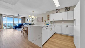 Eine moderne Wohnung mit Küche, Essbereich und Wohnzimmer. Sie verfügt über weiße Schränke, eine Marmorinsel und eine große Schiebeglastür zum Balkon.