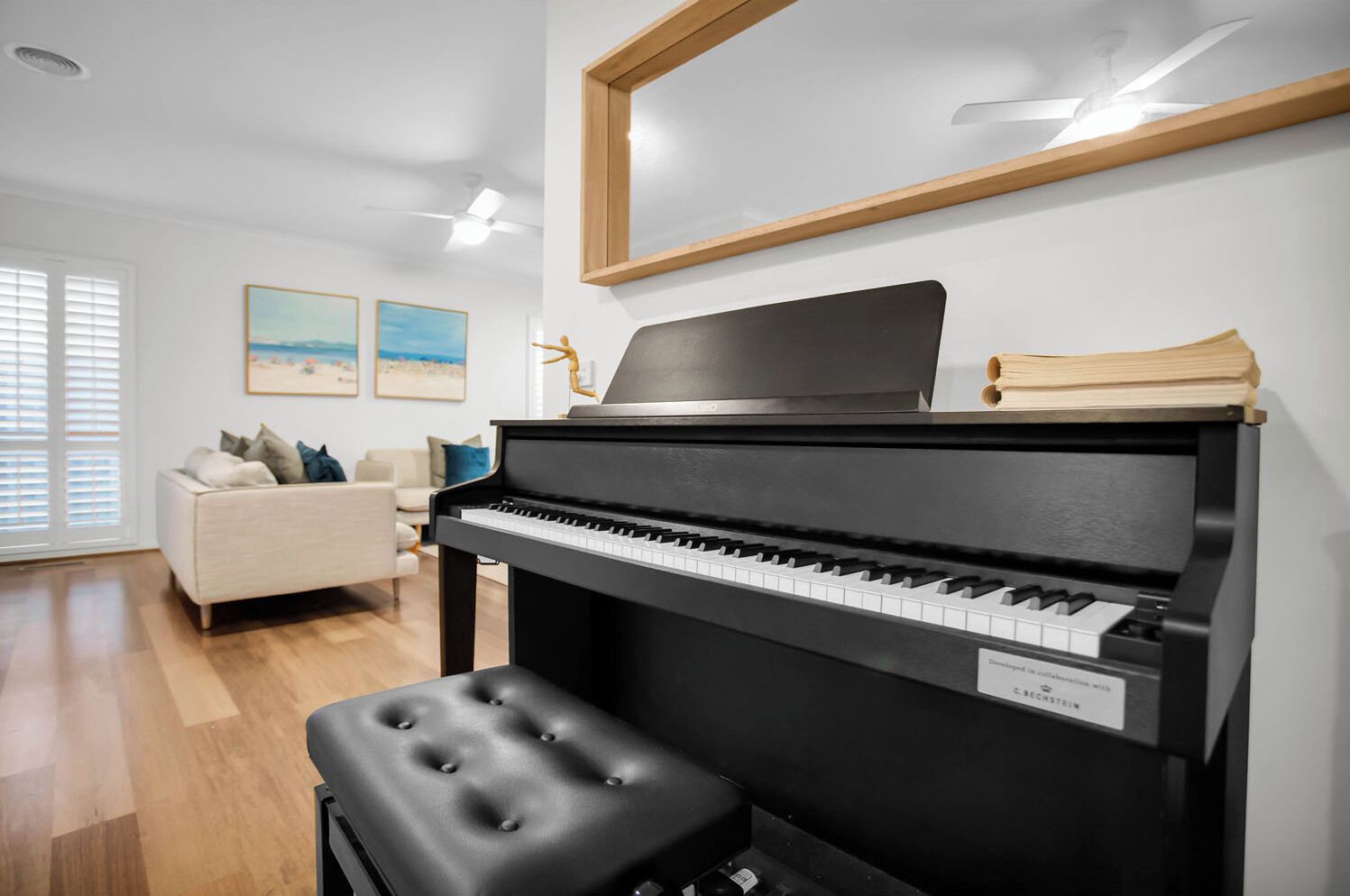 A modern living room with a black piano, a cushioned bench, a sofa, and a large window with blinds.