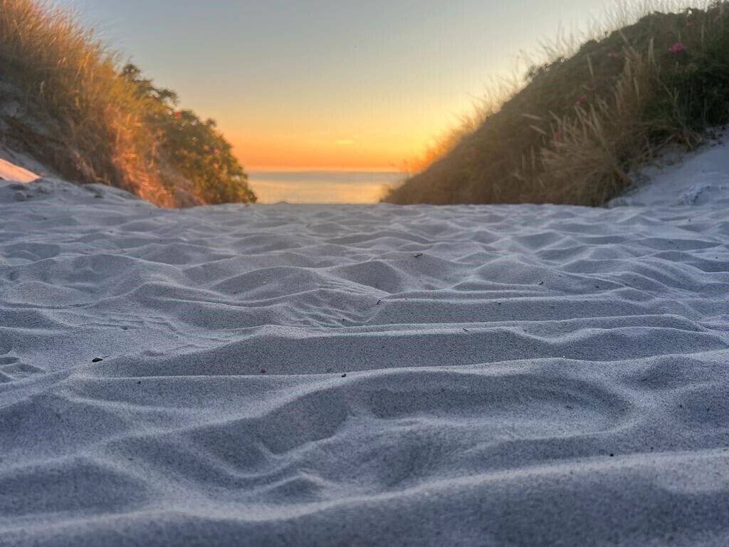 Une plage de sable avec des dunes aux contours doux et un coucher de soleil en arrière-plan.
