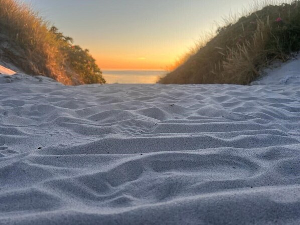 A sandy beach with undulating dunes and a sunset in the background.
