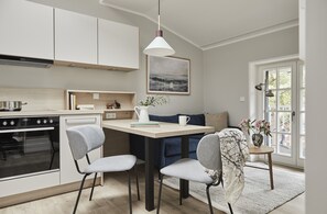 A modern kitchen with a dining area, featuring a built-in oven, a pendant light, and a view of the outdoors through a large window.