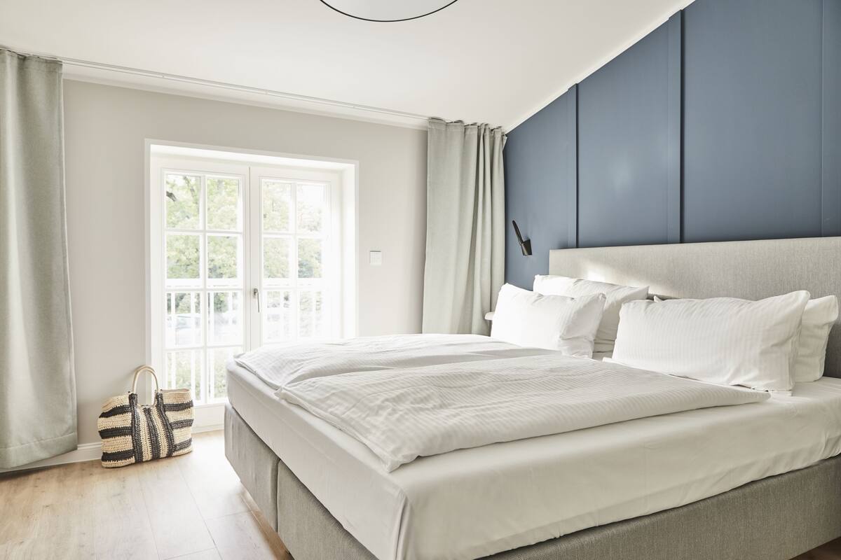 Un dormitorio con una cama grande, una ventana con cortinas y un bolso en el suelo.