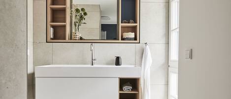 Een moderne badkamer met een grote spiegel, een witte wastafel en een ingebouwd schap.