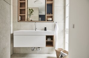 A modern bathroom with a large mirror, a white sink, and a built-in shelf.