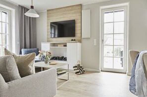 A modern living room with a flat-screen TV, a sofa, a coffee table, and a bookshelf.