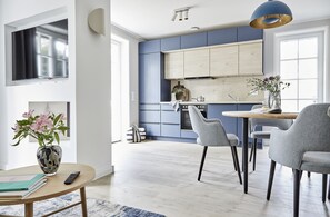 A modern kitchen with blue cabinets, a dining area with grey chairs, and a vase with flowers on the table.
