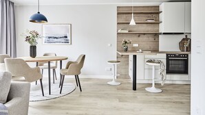 Et moderne køkken med hvide skabe, en træbordplade og en indbygget ovn. Der er et spiseområde med et rundt bord og stole, samt en barstol.