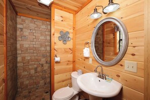 Et badeværelse i en træhytte med toilet, vask og brusebad.