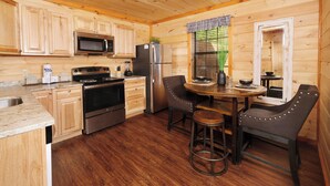 A wooden cabin kitchen with a stove, microwave, refrigerator, and bar stools. - Studio log cabin-convenient -pet friendly-hot tub- near PF parkway! (Pigeon Forge)