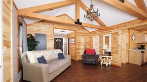 A cozy log cabin interior with a sofa, a small table, and a kitchen area. - Studio log cabin-convenient -pet friendly-hot tub- near PF parkway! (Pigeon Forge)