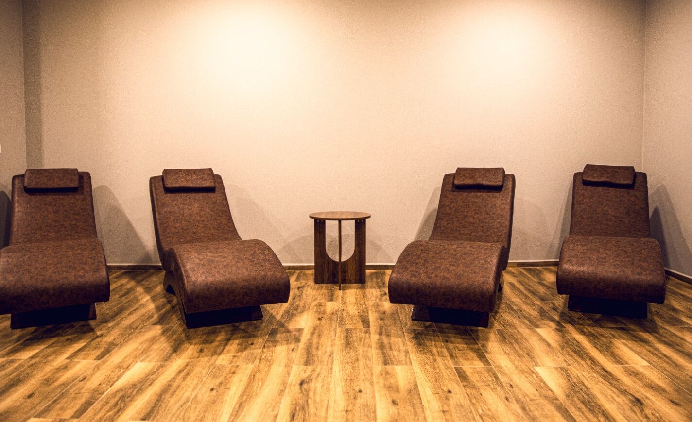 A room with four reclining chairs and a small table, with a wooden floor and a plain wall.