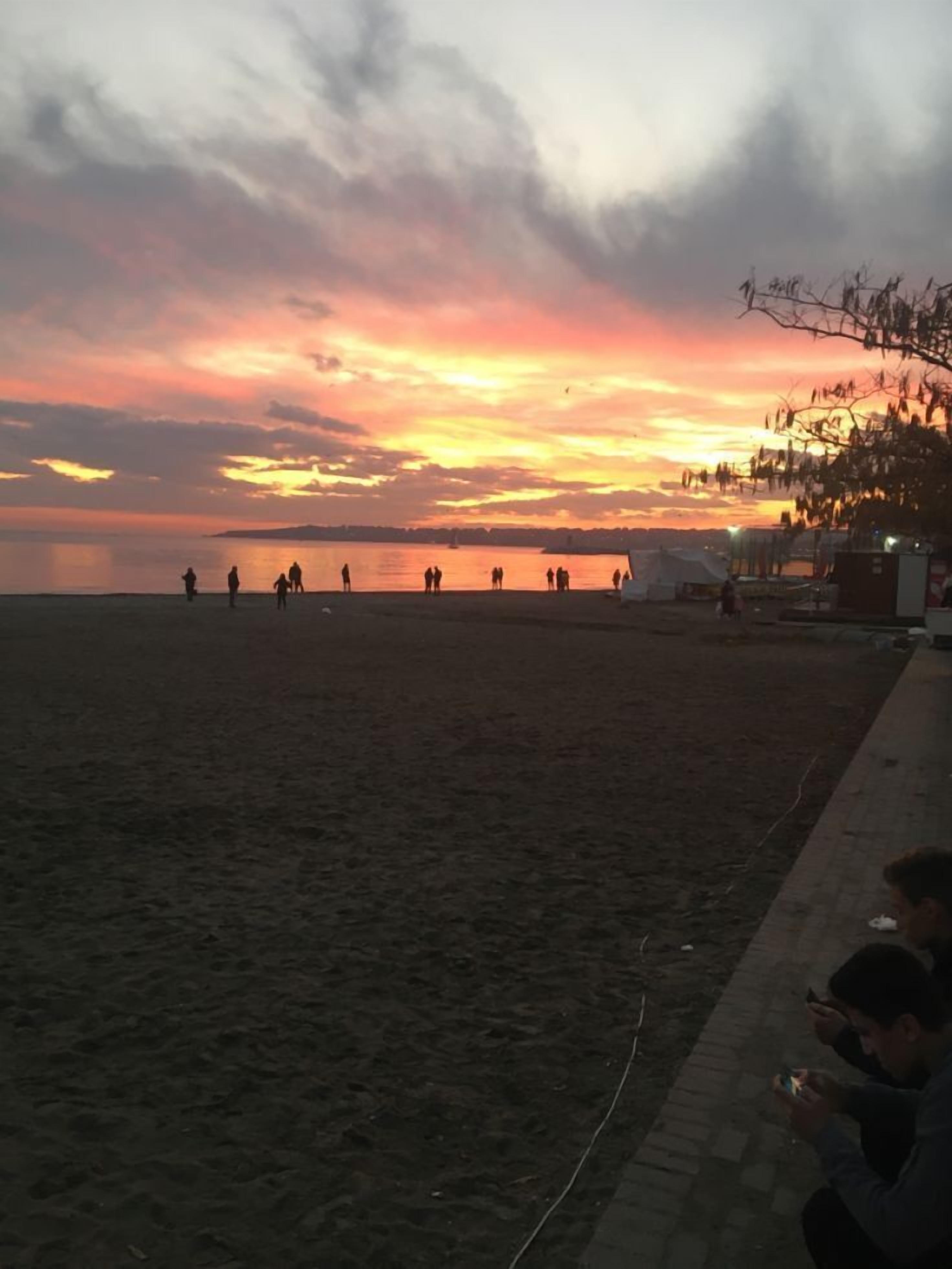 A beach at sunset with people walking along the shore.