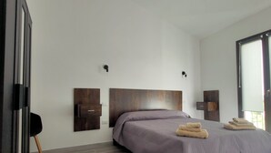A modern bedroom with a large bed, wooden headboard, two wall-mounted lights, and a large window. - Suite Apartments i4MORI Porto Pino (Sant'Anna Arresi)