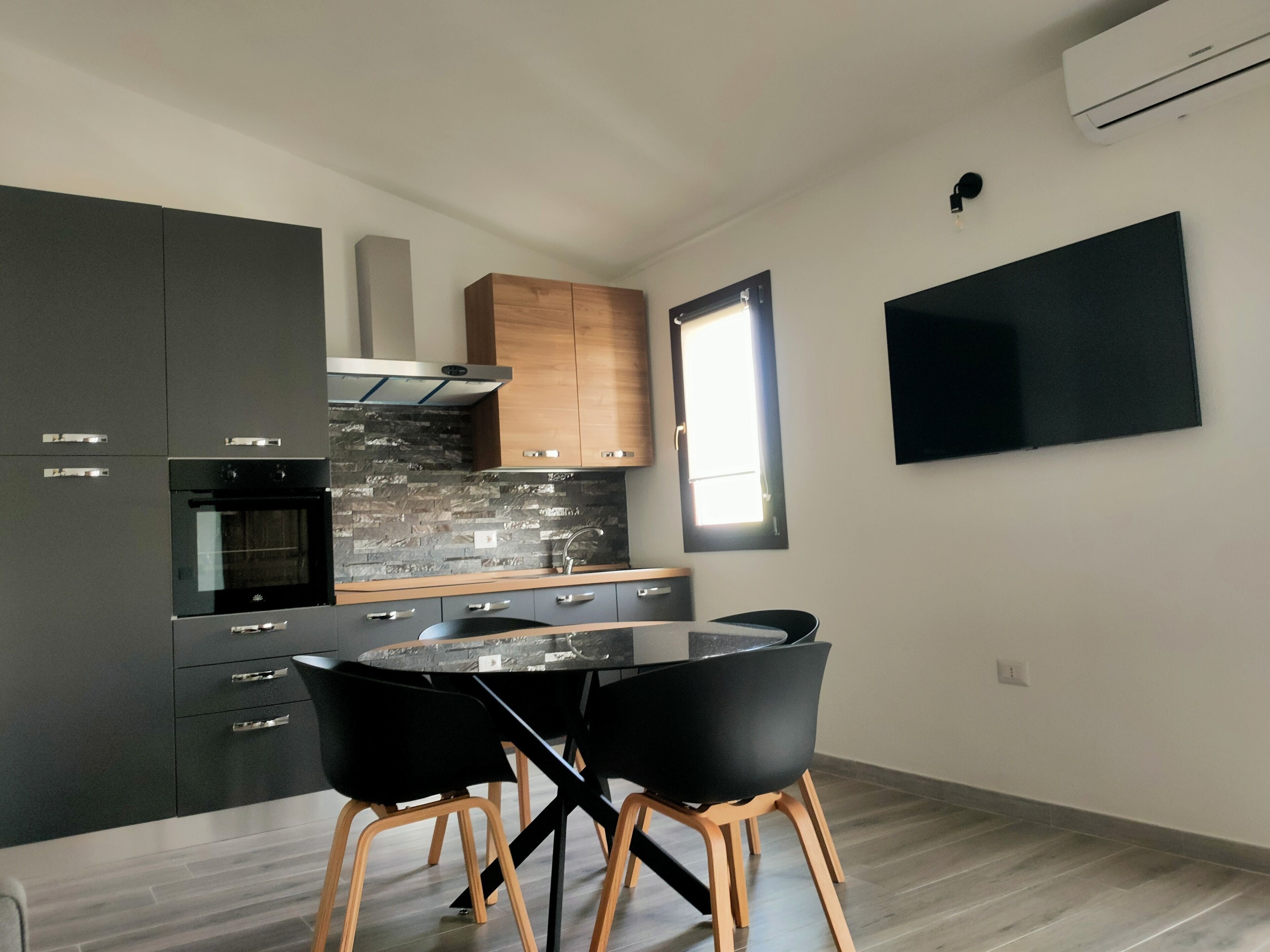 A modern kitchen with grey cabinets, a black oven, a wooden countertop, and a round dining table with black chairs.