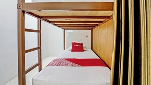 Un llit individual amb un coixí vermell amb l'etiqueta "OYO" i una manta amb dibuixos.