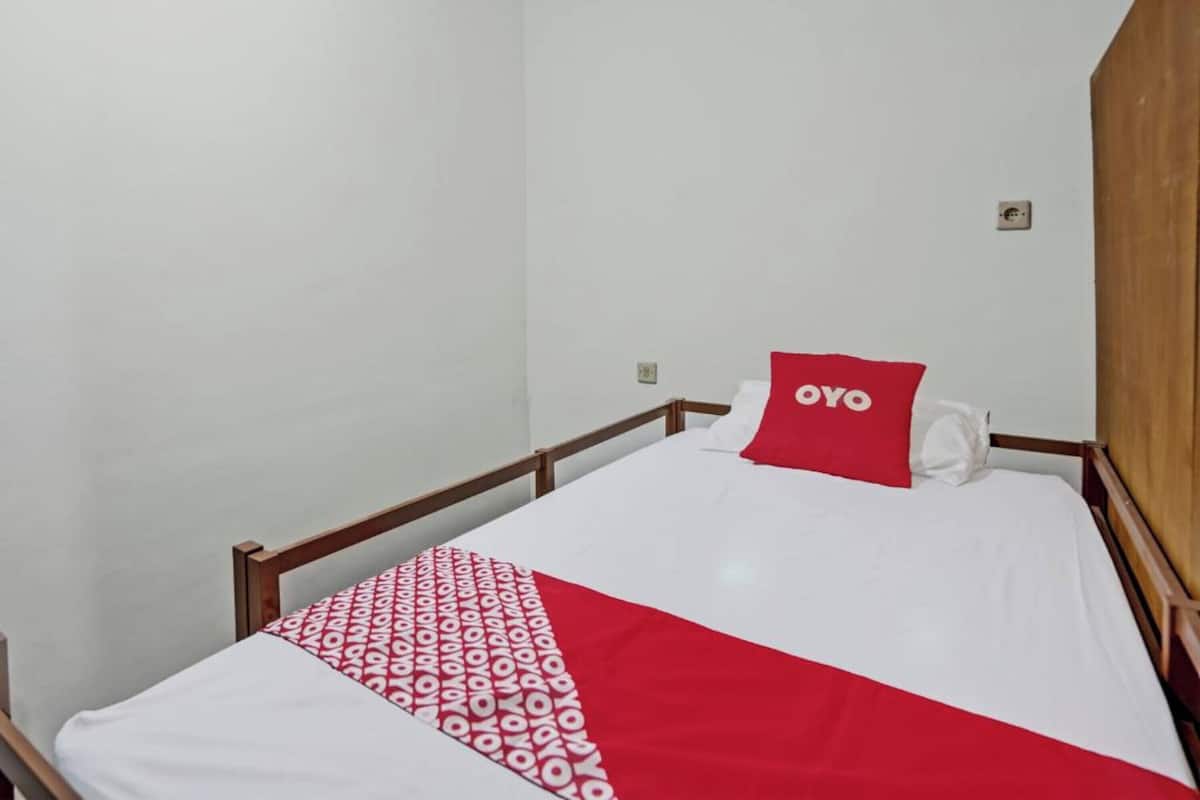 A single bed with a white and red bedspread, a red pillow with the text "OYO," and a wooden headboard.