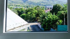Vista desde una ventana con marco triangular, que da a un valle con montañas, vegetación y edificios.