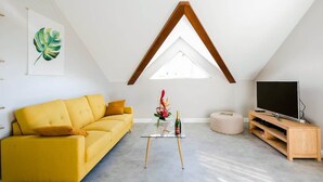 Una sala de estar moderna con un sofá amarillo, una mesa de centro de vidrio, un mueble de televisión de madera y un tragaluz.