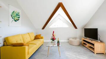 Un salon moderne avec un canapé jaune, une table basse en verre, un meuble TV en bois et une lucarne.