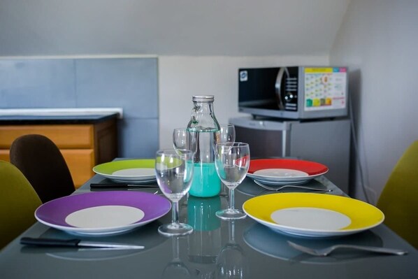 Une table à manger avec des assiettes colorées et des verres à vin, une bouteille en verre et un four à micro-ondes en arrière-plan.