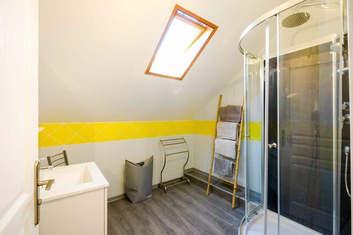 A bathroom with a skylight, a shower, a sink, and a towel rack.