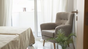 Una habitación con una cama, un sillón gris y una planta en maceta.