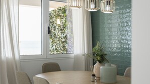 Un comedor con una mesa redonda, sillas, un jarrón con plantas y lámparas colgantes.