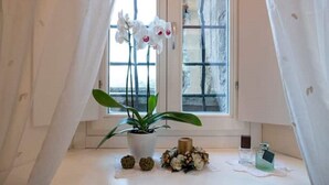 Une pièce avec une fenêtre, une plante en pot, une petite table et un flacon de parfum.