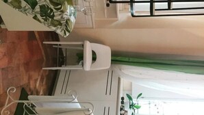 Une pièce avec une table blanche, une chaise blanche, une fenêtre avec un rideau vert et une vue sur un bâtiment à l’extérieur.
