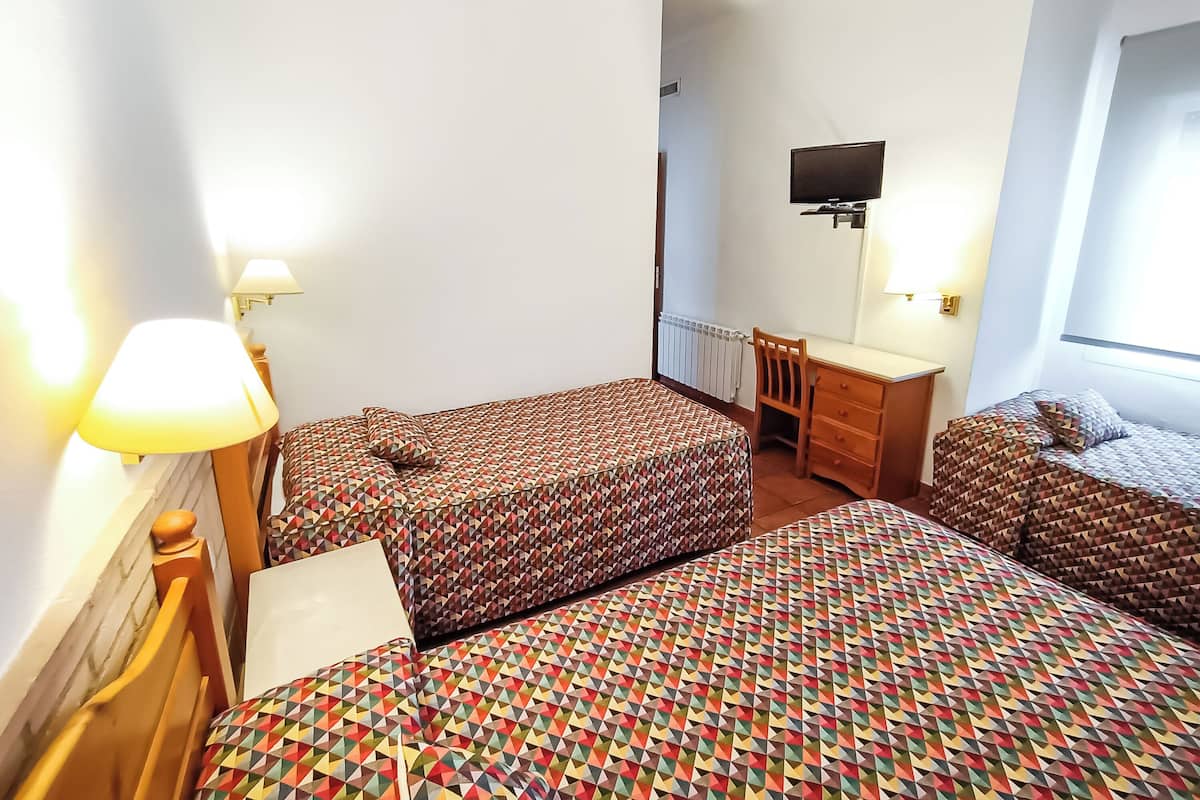 A hotel room with two beds, a desk, a chair, a TV, and a window.
