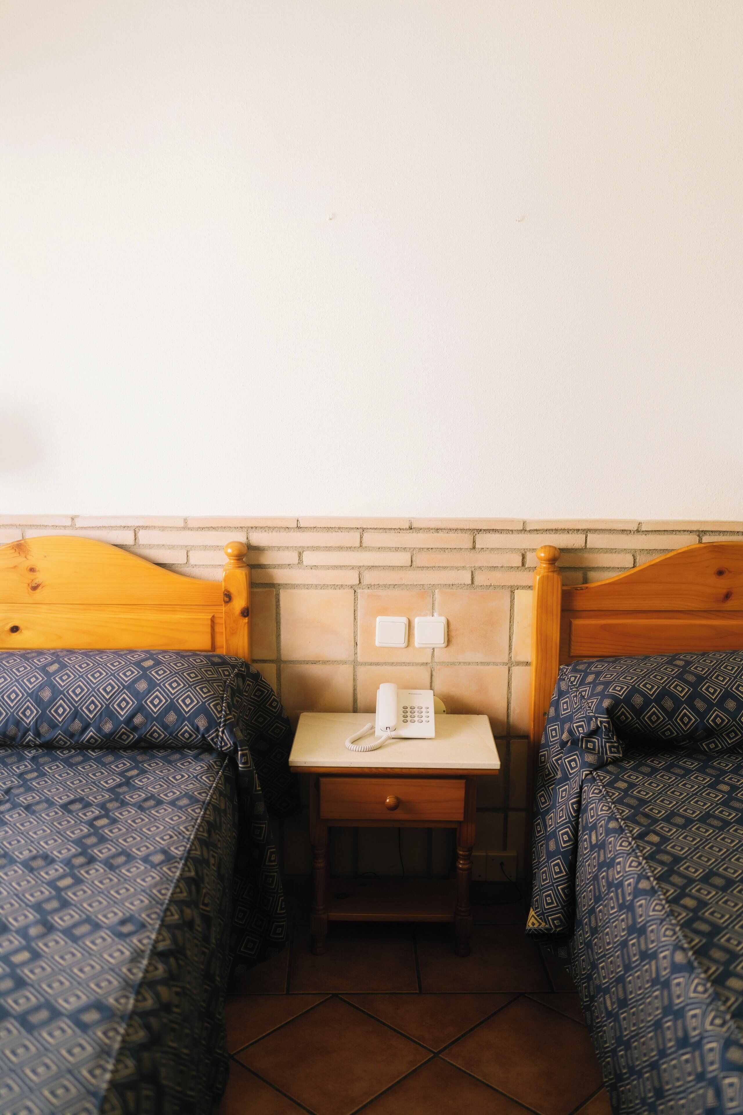 A small room with two beds, a nightstand, a telephone, and a brick-patterned wall.