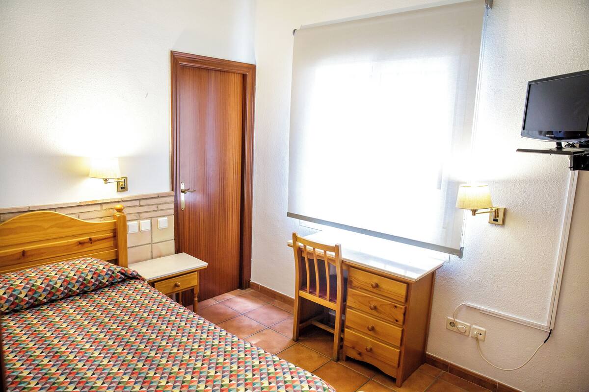 A bedroom with a bed, a desk, a chair, and a TV.