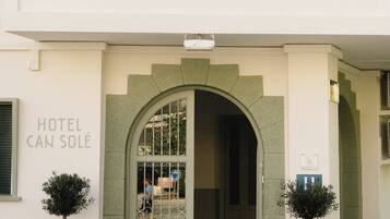 Entrada de un hotel con un gran arco, un letrero que dice "HOTEL CAN SOLÉ" y dos árboles en macetas a cada lado.
