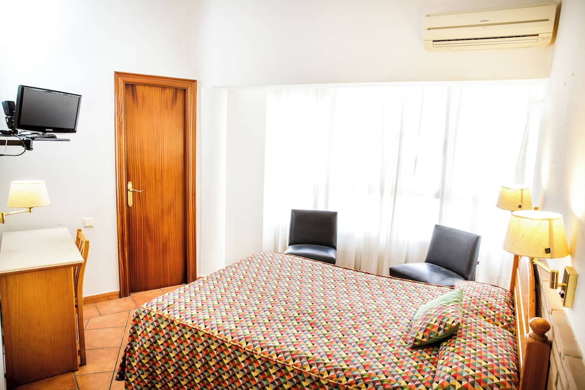 A hotel room with a bed, a desk, a chair, a television, and a window with curtains.