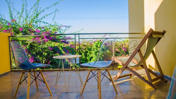 A balcony with two chairs and a small table, surrounded by a metal railing and a view of vibrant flowers. - Room-the White-orange Bedroom With a ple (Antananarivo)