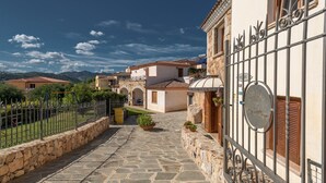 A stone-paved courtyard with a metal gate, surrounded by buildings with terracotta roofs and stone walls. - Stunning Residence Bouganvillage Studio Sleeps 2 Plus Child bed (Budoni)