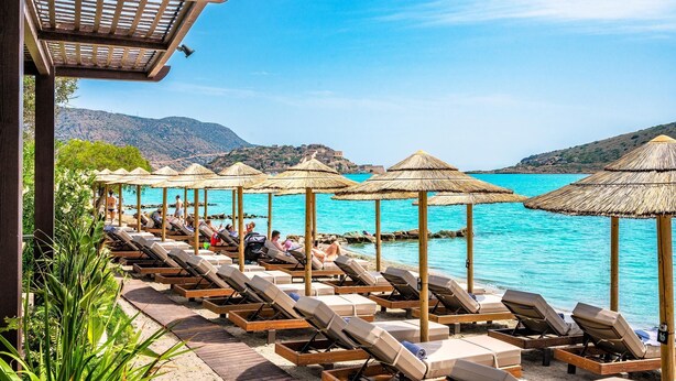 A beachside resort with sun loungers and thatched umbrellas, overlooking turquoise waters and hills. - Leyla Luxury Villa with Spinalonga View (Vrouchas)