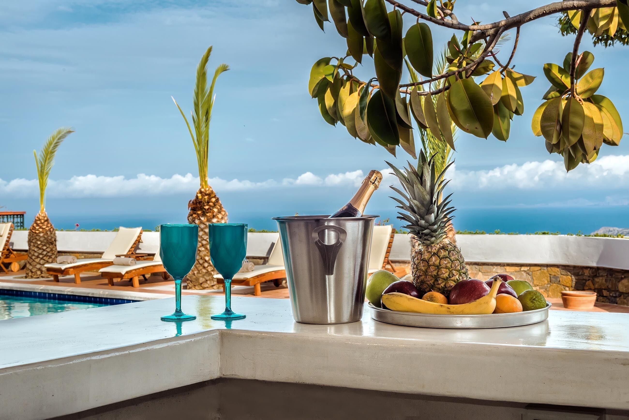 Un espace aménagé au bord de la piscine, avec des chaises longues, un panier de fruits, un verre à cocktail et un extracteur de jus.