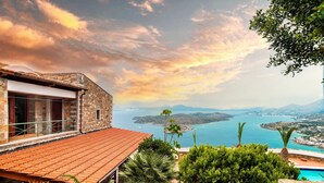 A stone building with a red-tiled roof, a pool, and a view of a lake and mountains. - Leyla Luxury Villa with Spinalonga View (Vrouchas)
