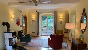 A spacious living room with a wooden floor, a ceiling fan, a fireplace, and a view through a glass door to the outdoors.
